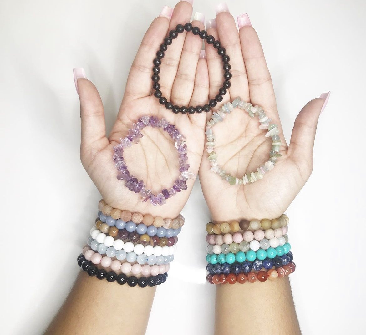 Hands holding crystal chip and bead bracelets, with stacks of bracelets on both wrists
